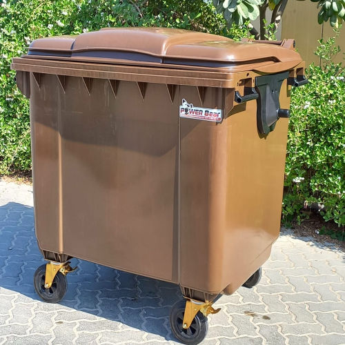 Large brown outdoor waste bin with wheels, placed on a paved area with green foliage in the background -  POWER Bear